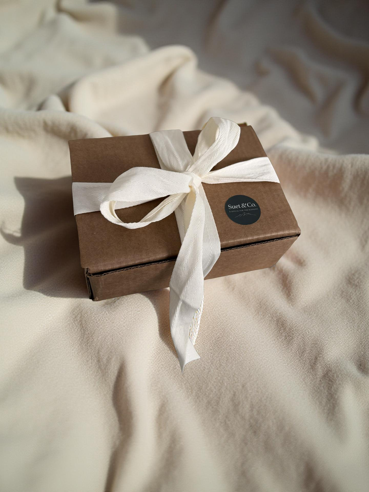 Brown gift box with a white ribbon on a beige fabric background