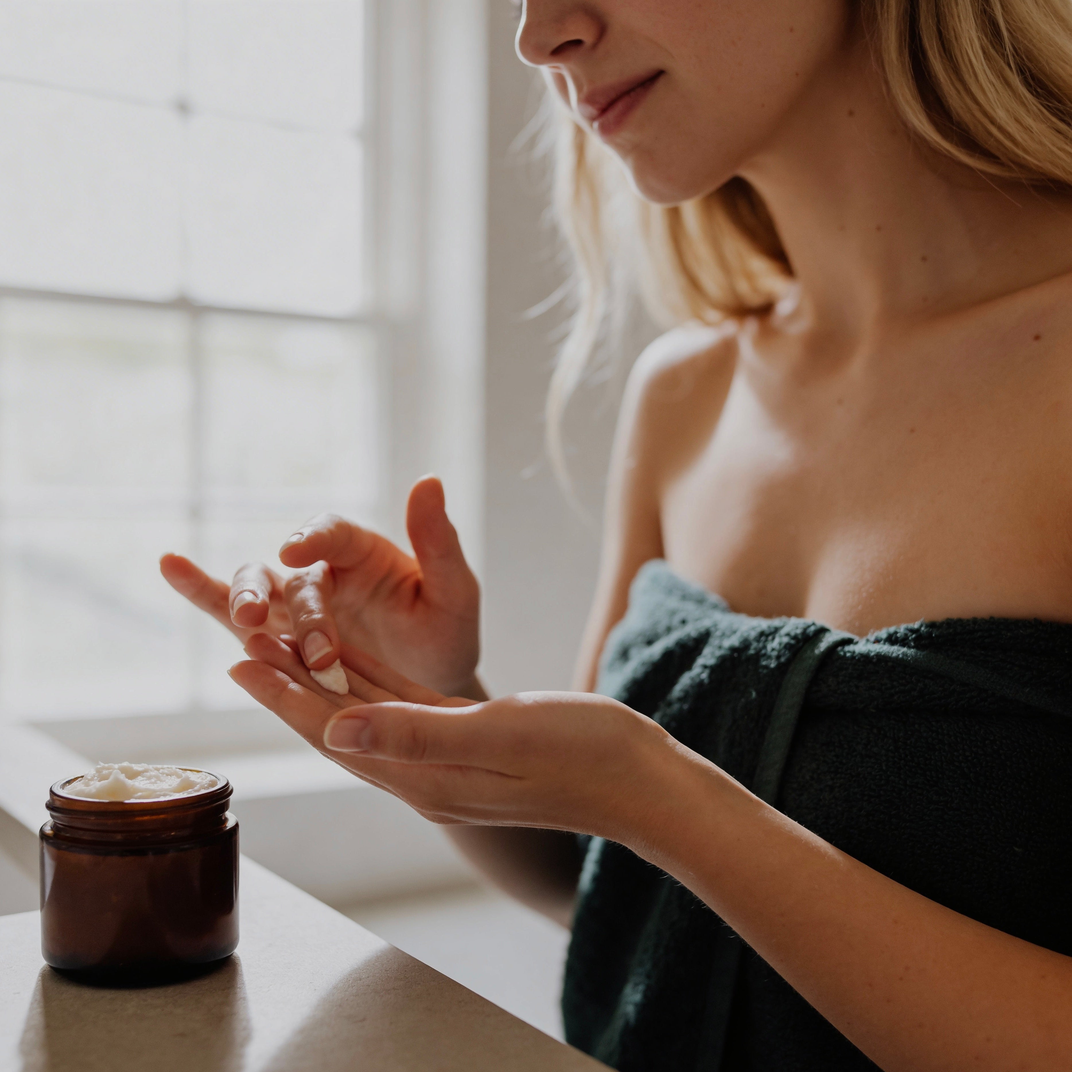 Woman applying Suet & Co. whipped tallow moisturizer to her hand with a jar of tallow on a surface.