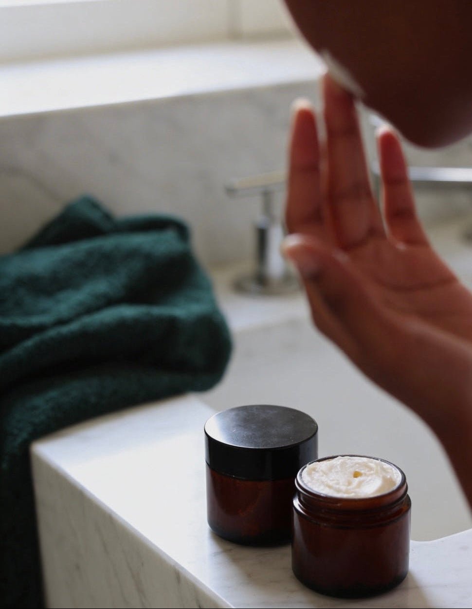 Person applying Suet & Co. whipped beef tallow moisturizer to face with two skincare products on a bathroom counter.