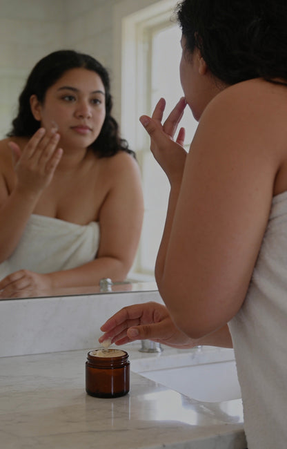 Woman applying Suet & Co. Veil to her face in front of a mirror
