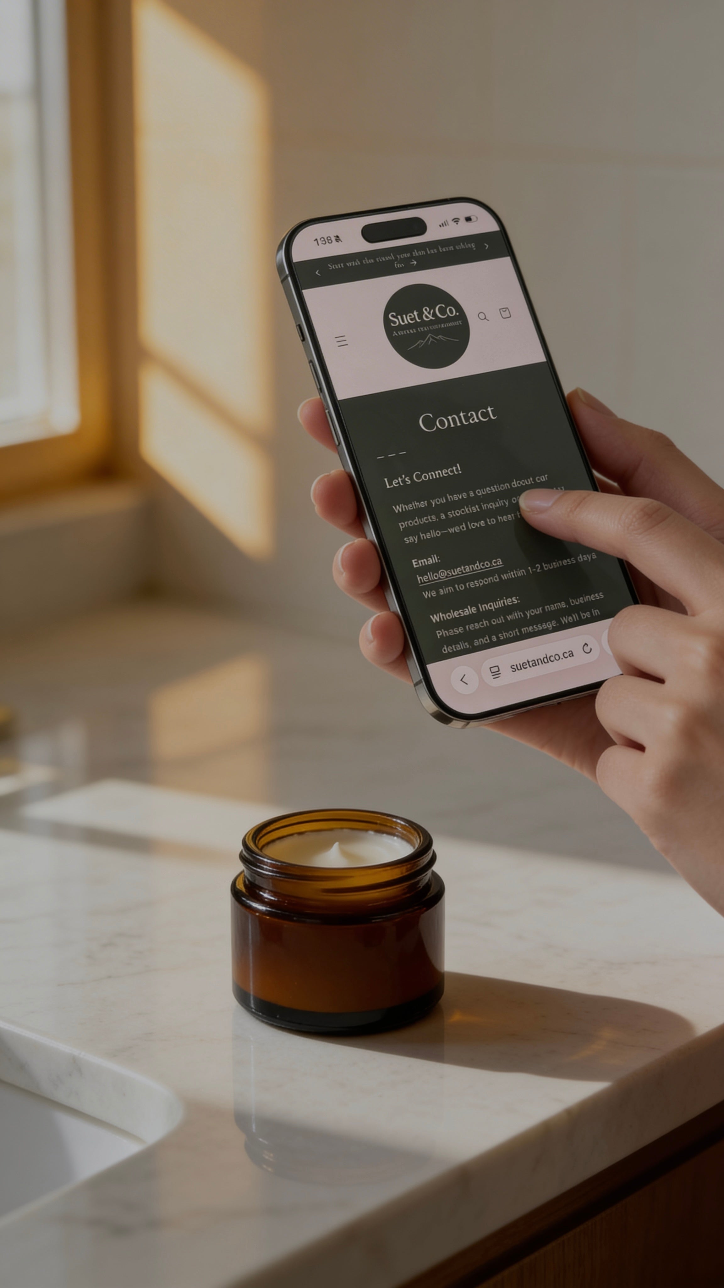 Person holding a smartphone with a website displayed, next to a small jar on a marble surface.